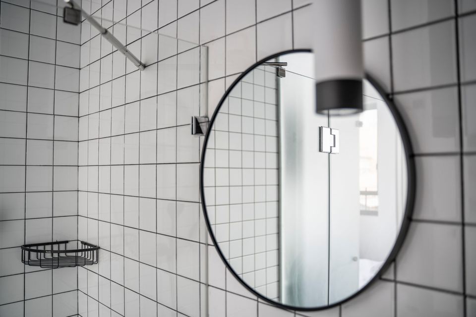 Bathroom with white tiles and a round black-framed mirror
