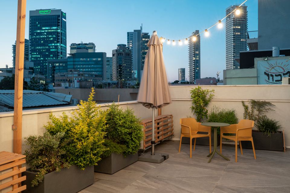 Hotel rooftop at dusk with string lights and the Tel Aviv skyline