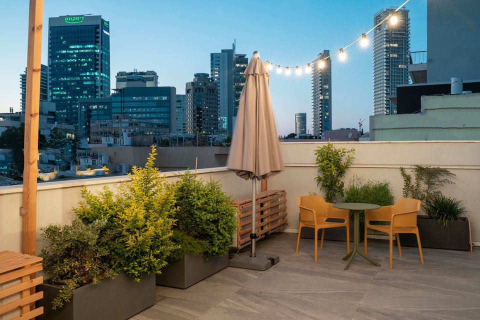Toit de l'hôtel au crépuscule, guirlandes lumineuses, parasol et skyline de Tel Aviv