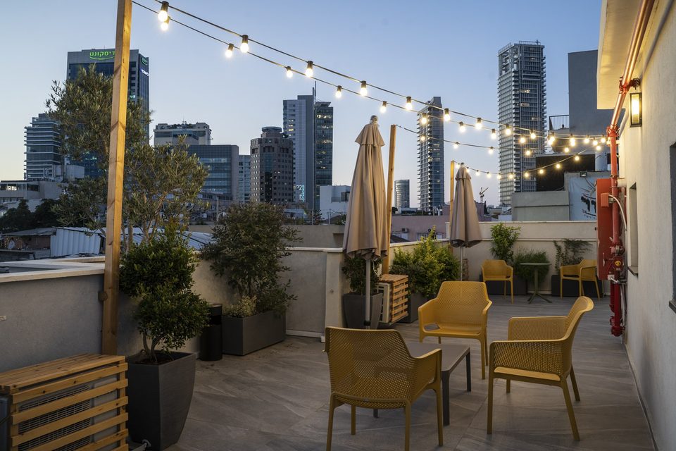 The rooftop at dusk with string lights and Tel Aviv towers