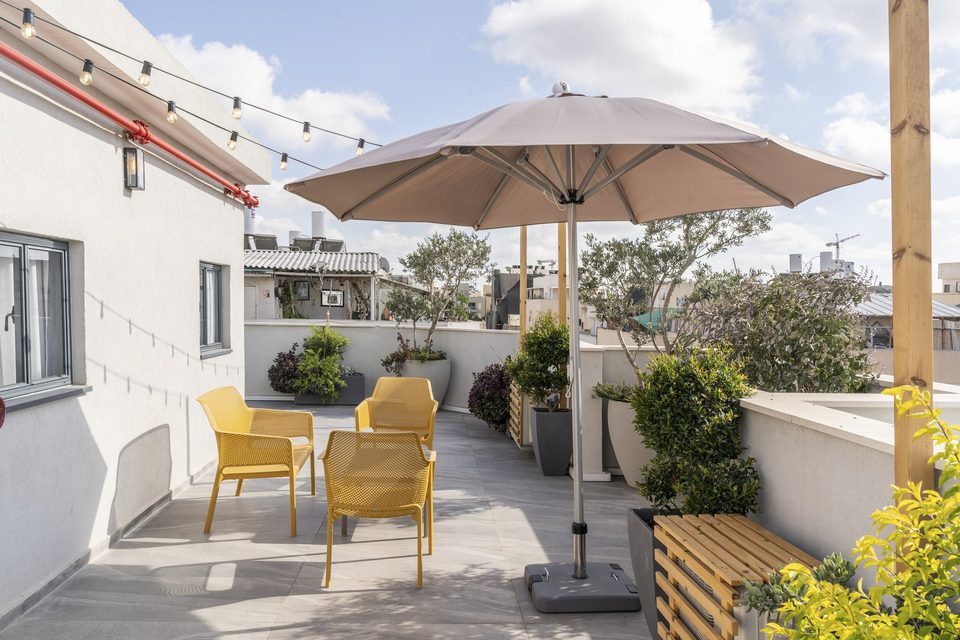 Toit ensoleillé de l'hôtel avec parasol, fauteuils jaunes et verdure